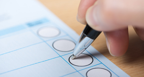 Hand mit Stift, die ein Kreuz auf einem Wahlzettel macht