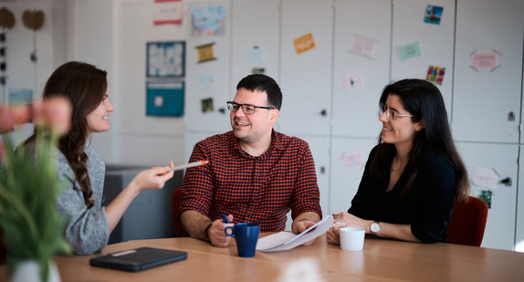 Zwei Frauen und ein Mann sitzen an einem Tisch im Lehrerzimmer und diskutieren