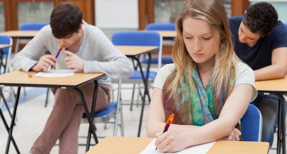 Eine Schülerin und hinter ihr sitzend zwei Schüler schreiben eine Prüfung