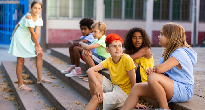 Gruppe von Jungen und Mädchen, die draußen auf der Schultreppe sitzen und plaudern