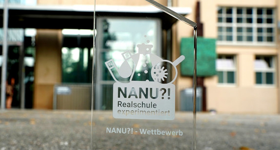 Auf durchsichtigem Grund steht Rrealschulpreis NANU?!", dahinter ist verschwommen ein Gebäude zu sehen. 