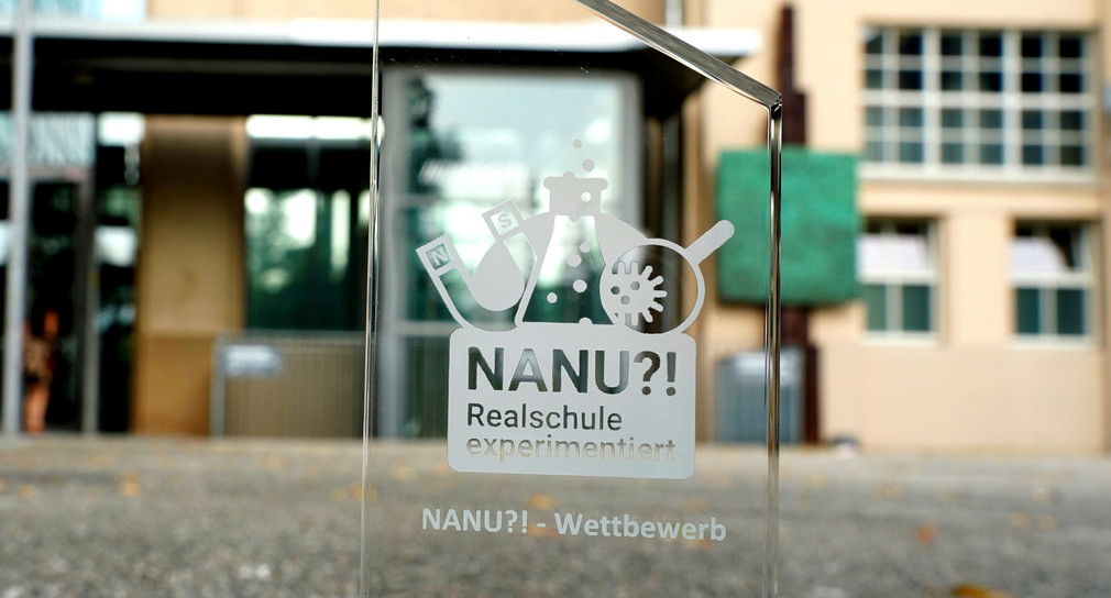 Auf durchsichtigem Grund steht Rrealschulpreis NANU?!", dahinter ist verschwommen ein Gebäude zu sehen. 