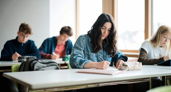 Schülerinnen und Schüler mit Stiften in der Hand an Schultischen