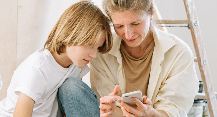 Eine Mutter und ein Sohn sehen sich Inhalte auf einem Smartphone an.
