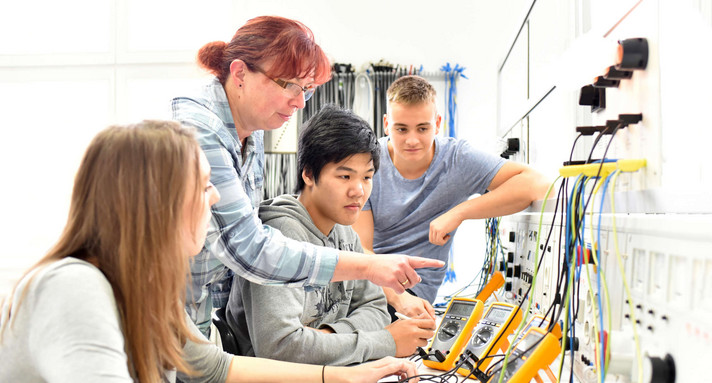 Eine Lehrerin erklärt zwei Schülern und einer Schülerin technische Geräte