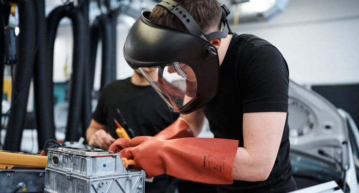 Ein Schüler mit Schutzbrille und Handschuhen in einer Autowerkstatt