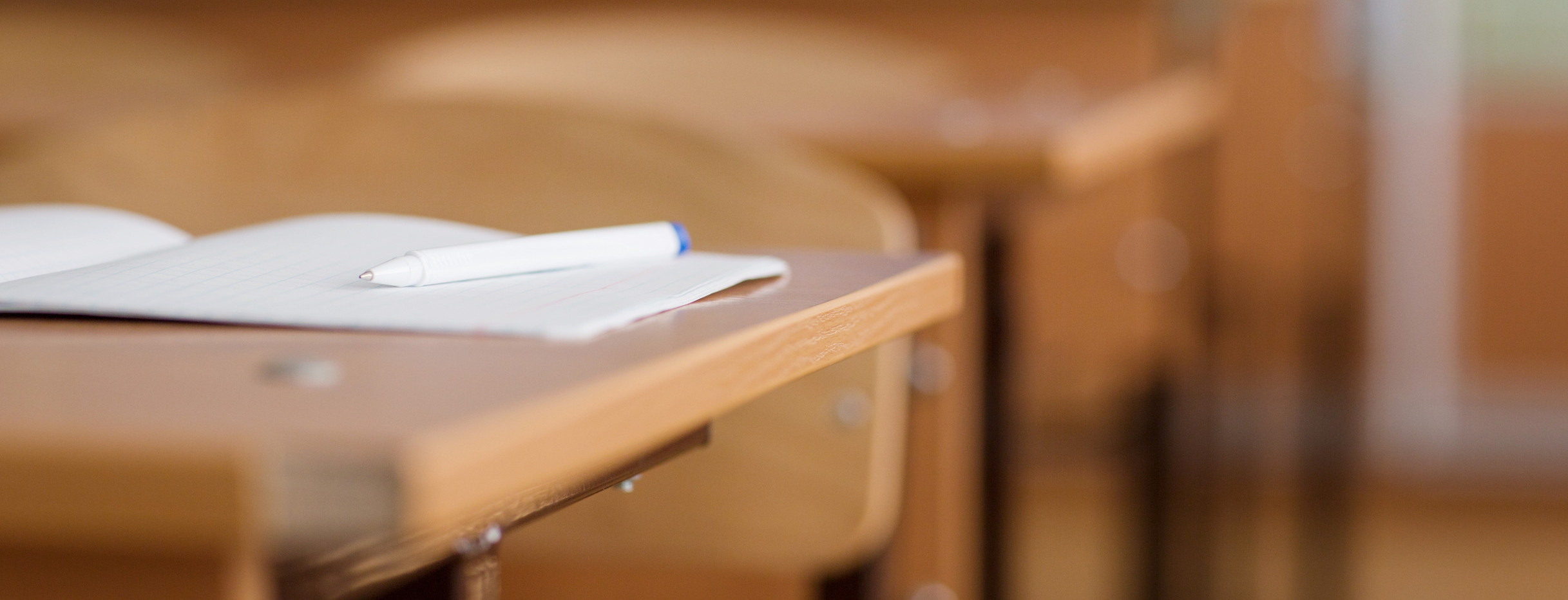 Schultisch, Notizbuch und Stift liegen auf dem Tisch. Der Rest der Schulklasse in Unschärfe