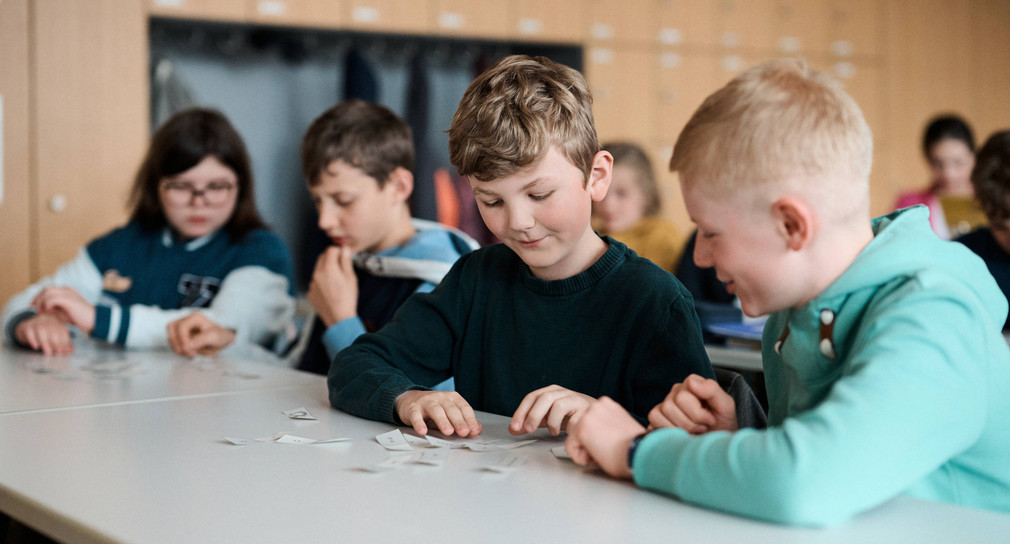 Schüler sitzen mit beschrifteten Karten an einem Schultisch