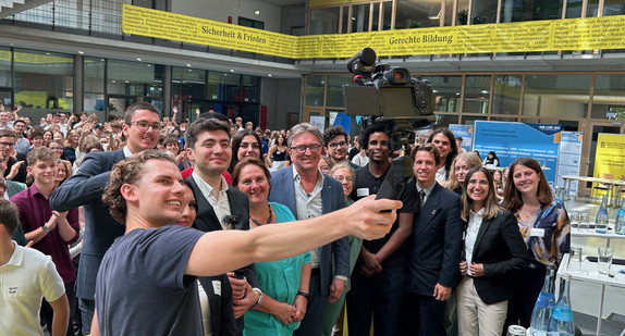 Eine Gruppe von Jugendlichen und Erwachsenen steht in einem großen Raum und von ihnen wird ein Foto gemacht. , 