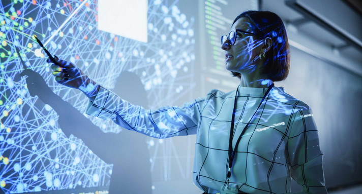 Young Female Teacher Giving a Data Science Presentation in a Dark Auditorium with Projecting Slideshow with Artificial Intelligence Neural Network Architecture. Business Startup and Education Concept