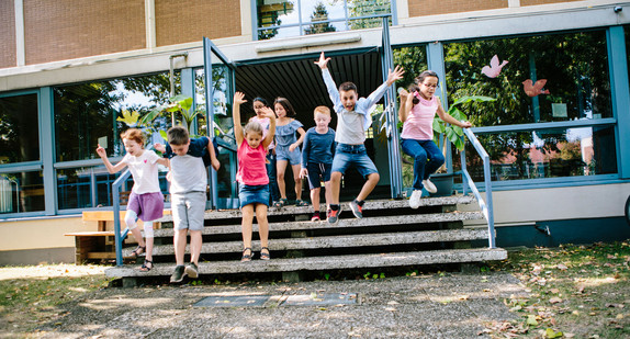 Grundschülerinnen und Grundschüler rennen fröhlich aus der Schule heraus