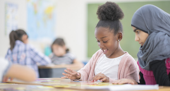 Zwei Mädchen mit Flüchtlingshintergrund sitzen zusammen im Klassenraum