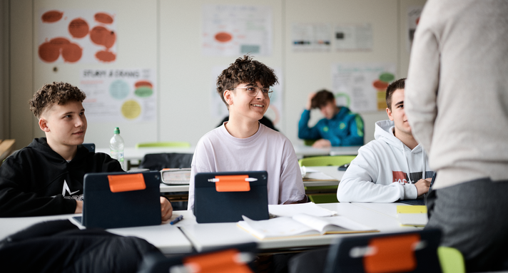 Schüler mit Tablets lauschen aufmerksam einer Lehrkraft