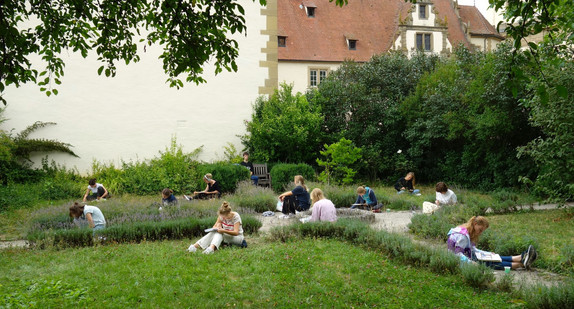 Schülerinnen und Schüler sitzen in einem Garten und schreiben Texte. 
