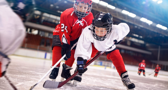 Jungen mit Schutzhelmen spielen Eishockey