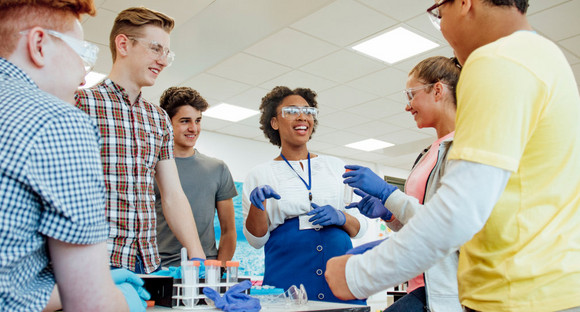 Eine Wissenschaftlerin und Jugendliche mit Schutzbrillen