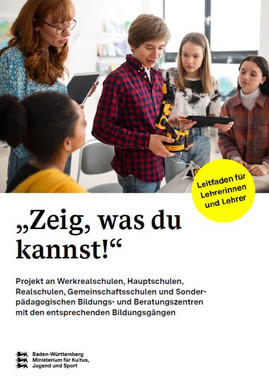 Vier Schülerinnen und Schüler stehen zusammen. Eine Lehrerin schaut ihnen über die Schulter. Alle betrachten einen Roboter, den der Schüler in der Mitte in der Hand hält.