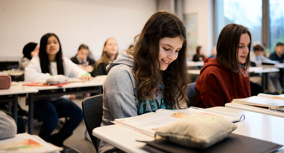 Schülerinnen und Schüler sitzen an Tischen in einem Klassenzimmer
