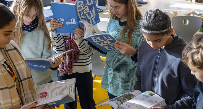 Schulkinder lesen im Schulbuch Baukultur.