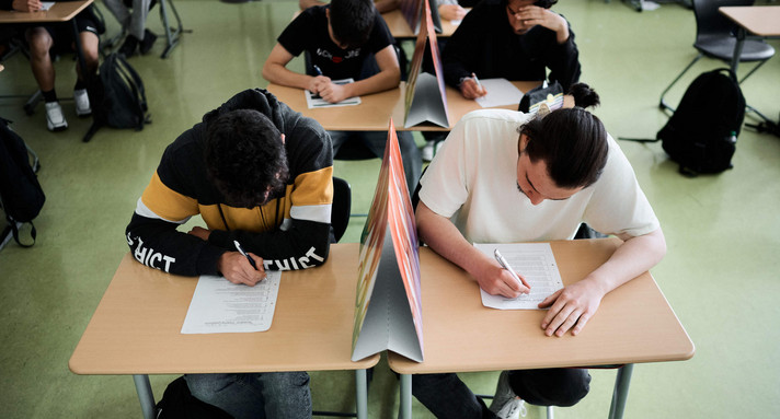 Schüler mit Abtrennungen zwischen den Schultischen bei einem Test