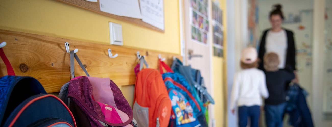 In einer Flur hängen an einer Wand viele bunte Kinderjacken. 