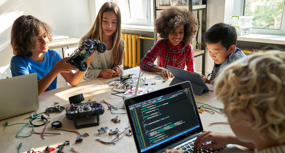 Schülerinnen und Schüler mit Laptops und Tablets arbeiten an selbstgebauten Robotern