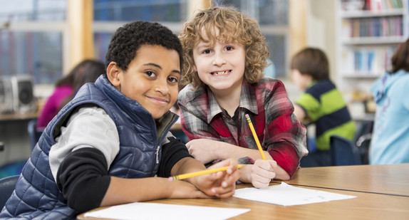 Zwei lachende Schüler unterschiedlicher Ethnien an ihrem Klassentisch