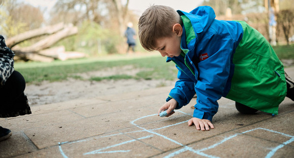 Ein Junge malt mit blauer Kreide auf den Straßenboden