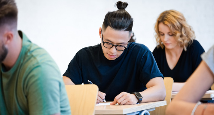 Schülerinnen und Schüler im Erwachsenenalter im Klassenraum bei konzentriertem Arbeiten