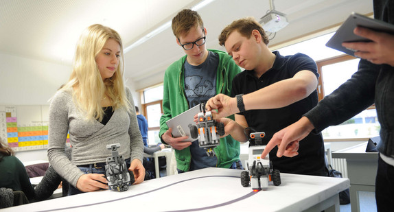 Schüler und eine Schülerin mit Robotern und Tablets in einem Unterrichtsraum