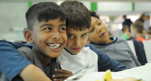 Drei Schüler mit Flüchtlingshintergrund in der Schulkantine sitzend, lachend und sich umarmend
