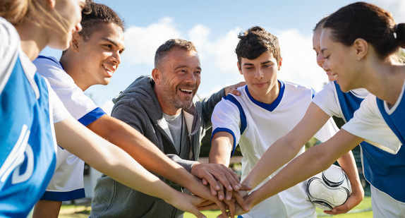 Team junger Fußballerinnen und Fußballer und der Trainer stapeln vor dem Spiel lachend die Hände