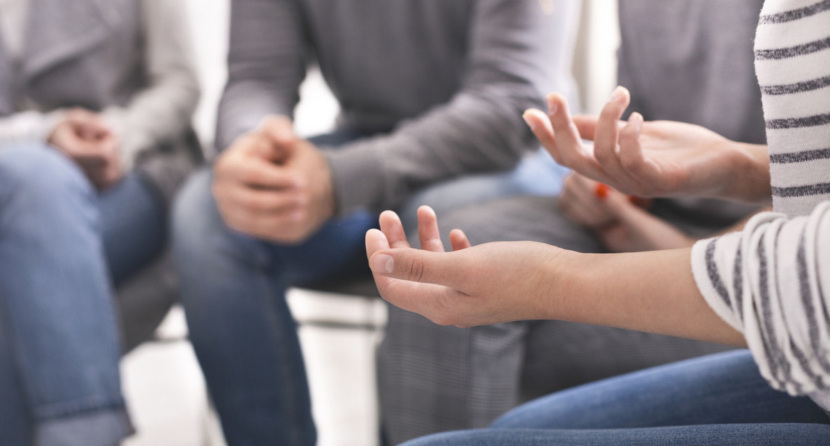 Eine Gruppe sitzt in einer Besprechung zusammen. Im Bild sind nur die unteren Körperhälften und die Arme und Hände zu sehen.