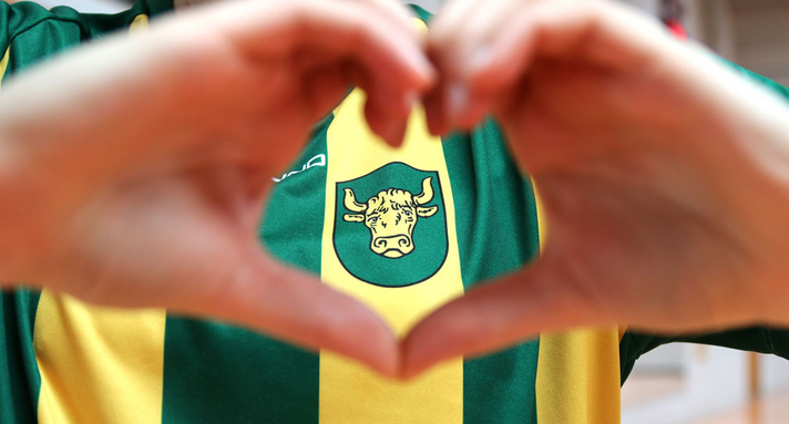 Ein Kind trägt ein gestreiftes Trikot und zeigt mit den Händen ein Herz. 