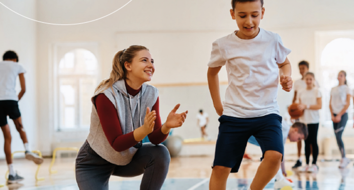 Eine Sportlehrerin unterstützt einen Jungen beim Schulsport.