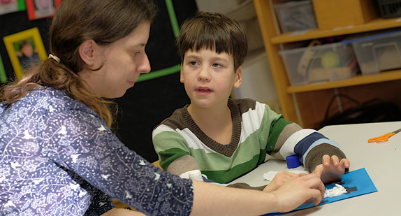 Lehrerin hilft Jungen mit Behindunger am Klassentisch
