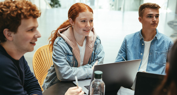 Ein junge Frau und zwei junge Männer sitzen mit Laptops an einem Tisch