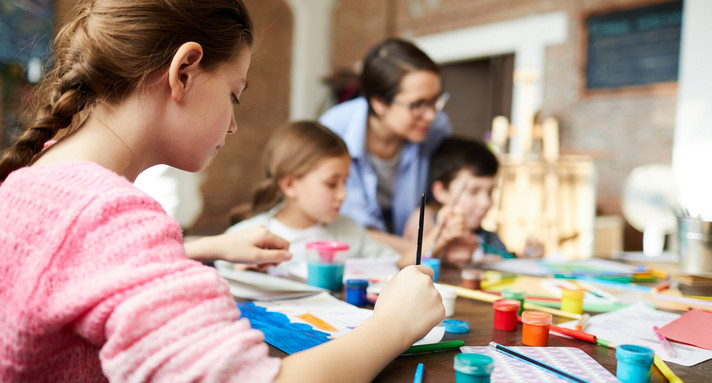 Kinder und eine Lehrerin mit Malutensilien an einem Tisch