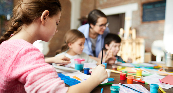 Kinder und eine Lehrerin mit Malutensilien an einem Tisch