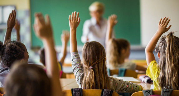 Back view of elementary students raising their arms on a class.