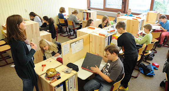Klasse in einer Gemeinschaftsschule. Jede Schülerin und jeder Schüler hat einen abgetrennten Bereich mit Regal für Ordner, um ungestörter Arbeiten zu  können