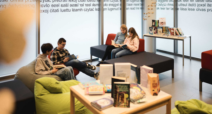 Schülerinnen und Schüler mit Büchern in einem Leseraum mit Sitzsäcken und Sofas