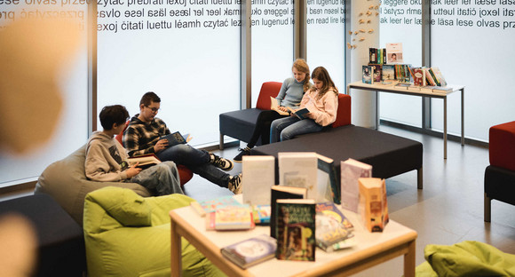 Schülerinnen und Schüler mit Büchern in einem Leseraum mit Sitzsäcken und Sofas