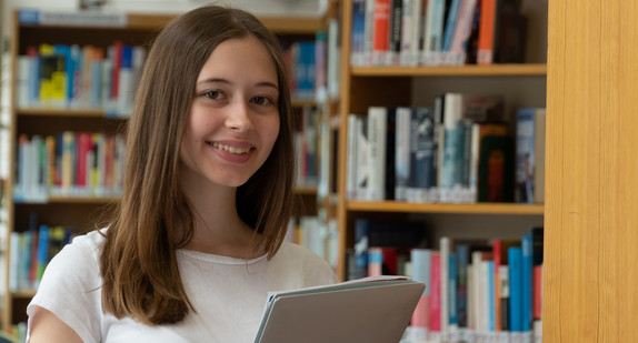 Teenagermädchen vor Regalen in der Schulbibliothek posierend