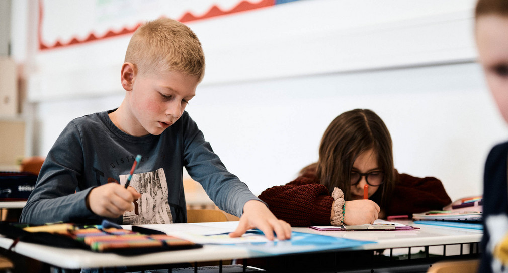 Ein Schüler und eine Schülerin mit Stiften an einem Schultisch
