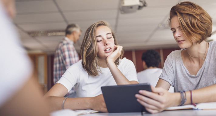 Schülerin und Schüler, die ein digitales Tablet im Klassenzimmer verwenden und diskutieren.