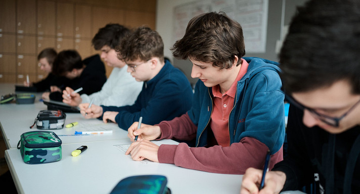 Sechs Schüler sitzen an einem Tisch nebeneinander in der Schule und schreiben etwas