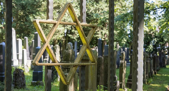 Ein David-Stern aus Metall an einem Friedhofszaun.  