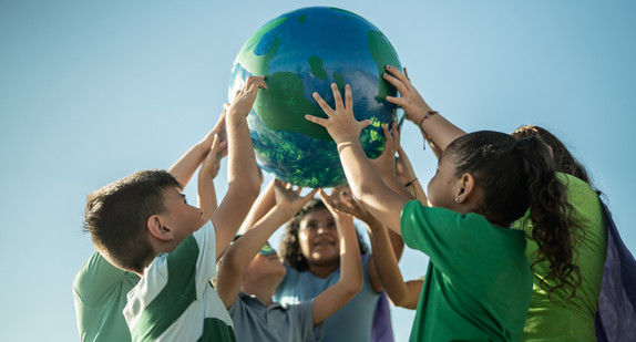 Im Kreis stehende Kinder halten gemeinsam einen Globus mit gestreckten Armen in die Höhe