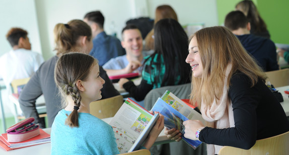 Zwei Schülerinnen unterhalten sich im Klassenraum wärhend des Unterrichts und tauschen sich zu dem Erlernten aus.